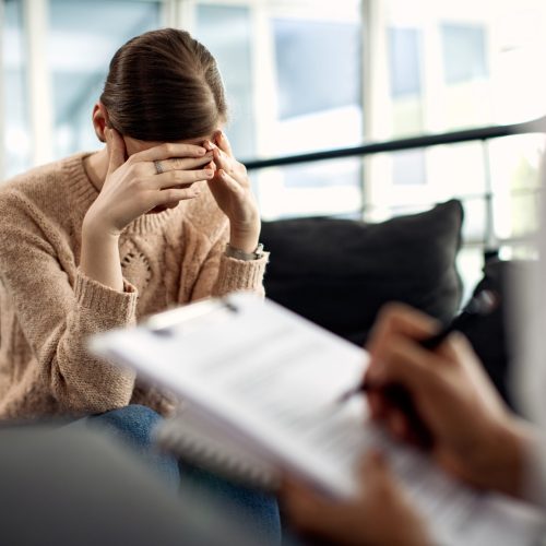 Sad woman holding her head in pain while having a meeting with psychotherapist.